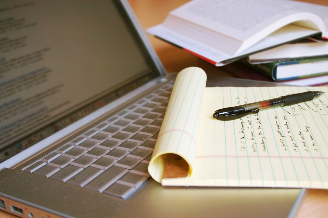 Photo of a laptop and writing pad